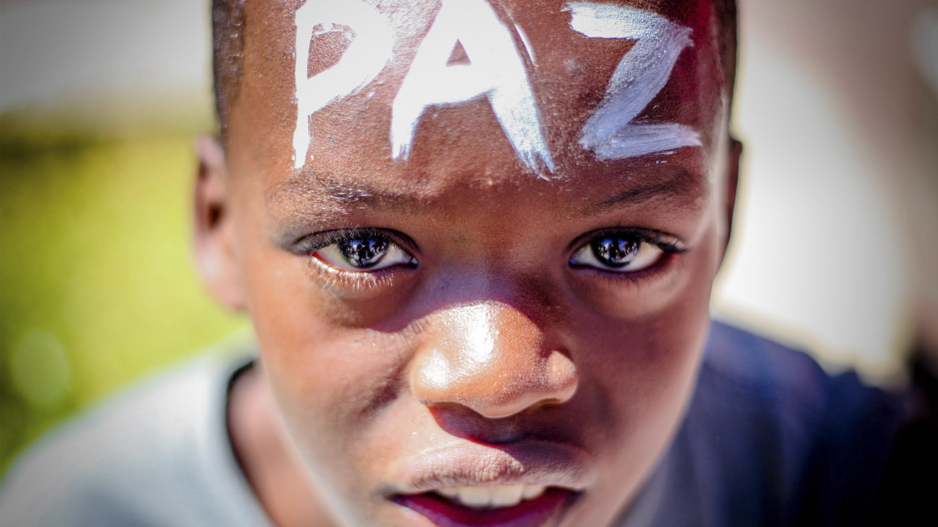 Foto de menino negro com a palavra paz escrita com tinta branca em sua testa