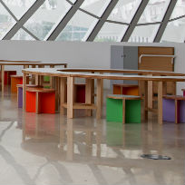 Foto do terreiro das curiosidades no Museu do Amanhã. Espaço vazio todo branco com cadeiras e mesas baixas coloridas.  | Foto: Bernard Lessa