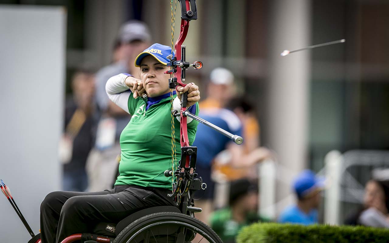 Atleta paralímpica atira flecha com arco em cima de sua cadeira de rodas