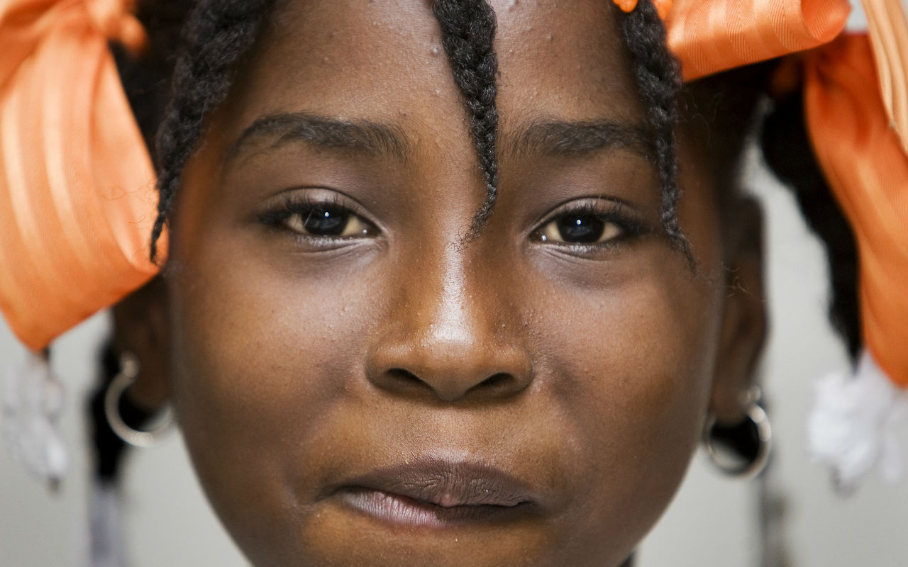 Criança negra sorrindo de frente para a câmera com laços laranjas no cabelo / Foto: UN Photo/Marco Dormino CC BY-NC-ND 2.0