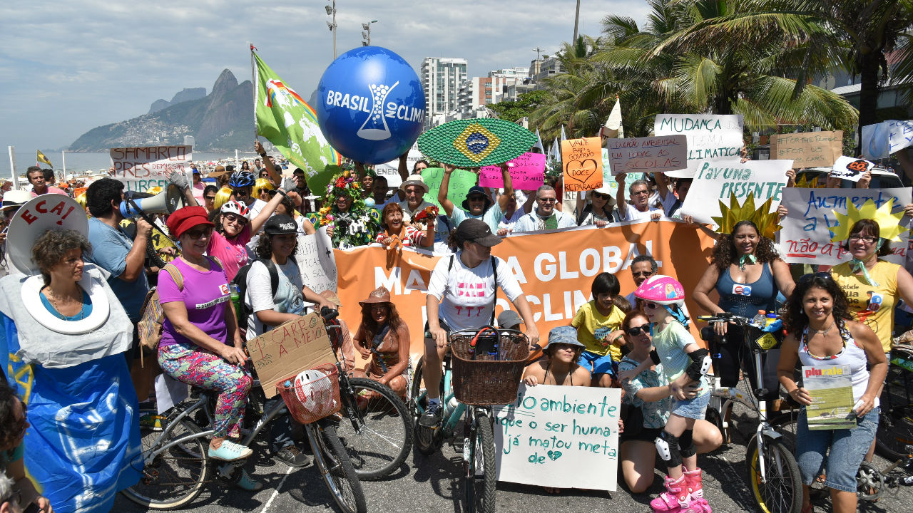 Homens e Mulheres na rua, alguns de bicicleta, segurando cartazes no ato da Marcha Mundial pelo Clima