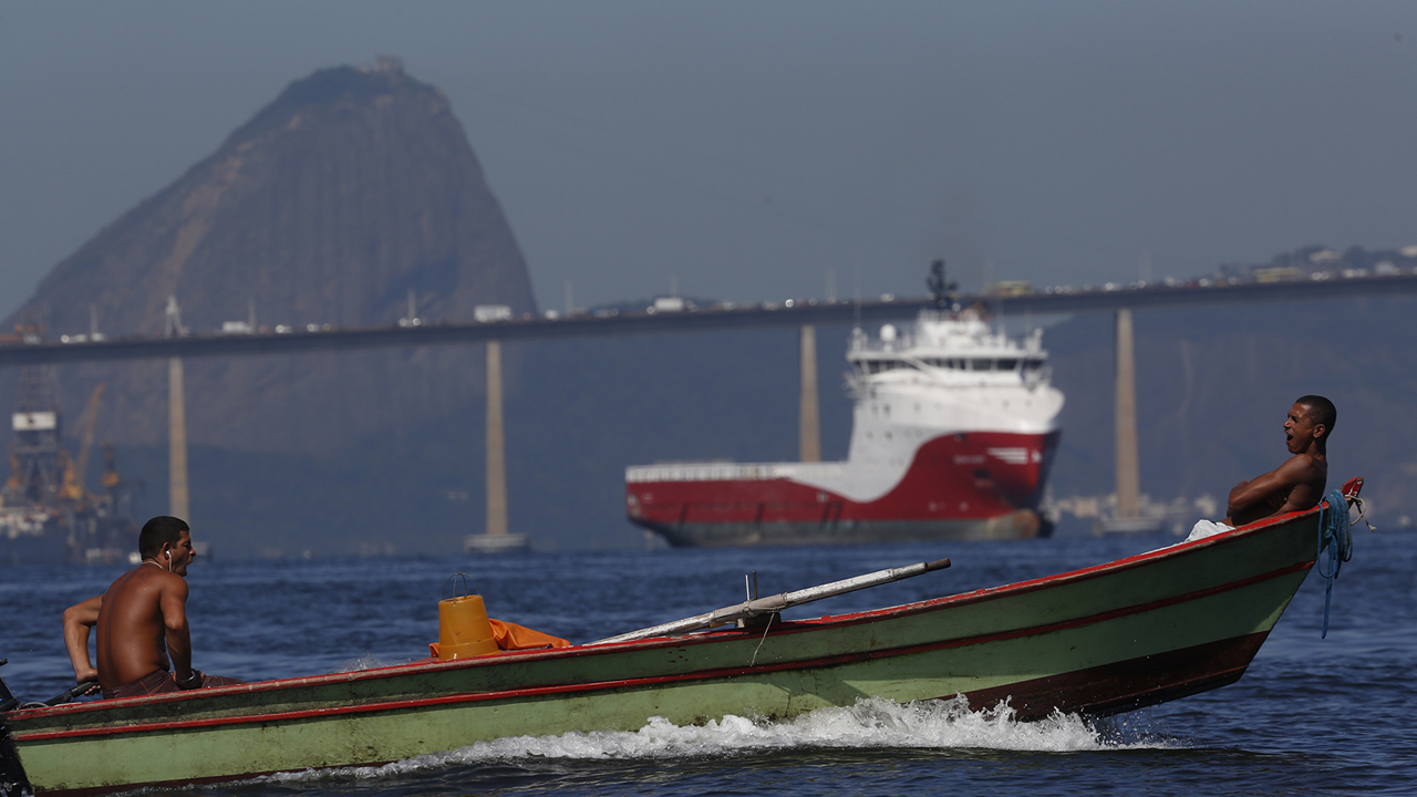 Dois homens em um pequeno barco na Baía de Guanabara com o Pão de Açúcar ao fundo