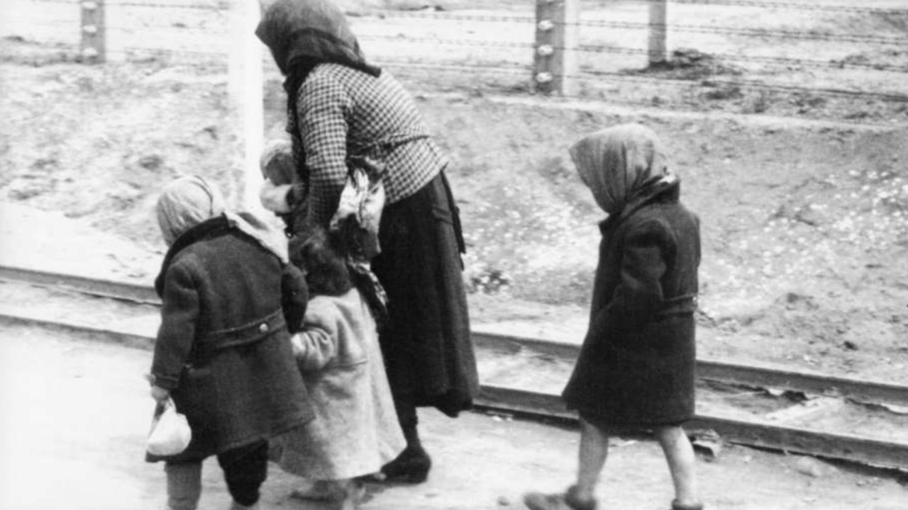 Senhora de costas andando de mãos dadas com duas crianças e uma terceira criança andando atrás delas