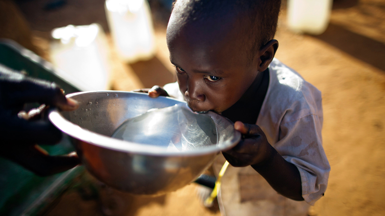 Criança negra bebendo água em uma tigela prata