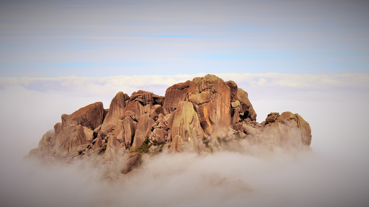 Topo de um rochedo envolvido por nuvens e neblina