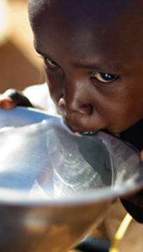 Criança negra bebendo água em uma tigela prata