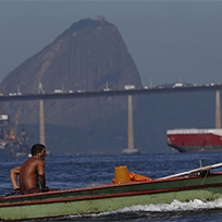 Homem em um pequeno barco na Baía de Guanabara com o Pão de Açúcar ao fundo