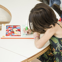 Menina sentada e escrevendo apoiada em uma mesa em um quadro em branco