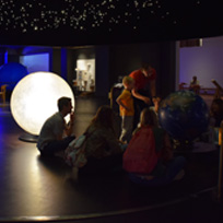 Grupo de pessoas realizando uma visita ao Science Museum, sentadas enquanto uma pessoa aponta para um globo