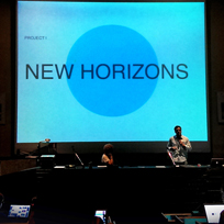 Nosso pesquisador do Observatório do Amanhã, Davi Bonela, em um palco de um auditório apresentando seu projeto. Ao fundo uma tela escrito "New Horizons".